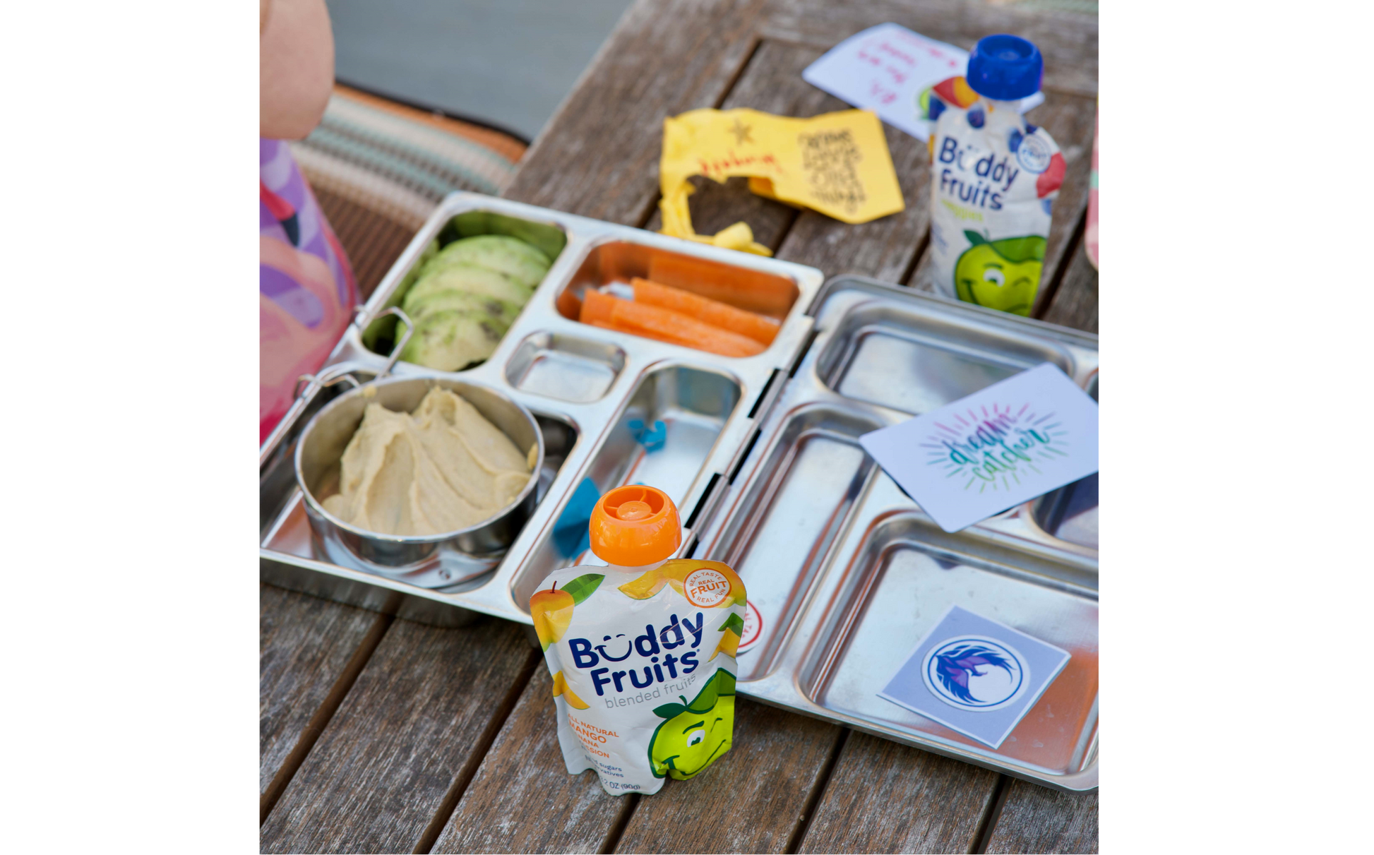 A child's lunch is accompanied by a tropical flair from the Buddy Fruits Mango, Banana, & Passionfruit fruit pouch.